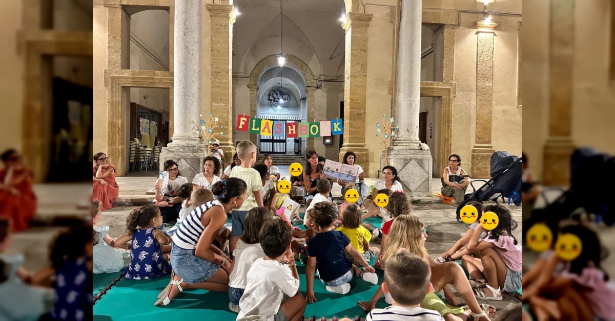 Bambini e famiglie seduti all'aperto con cuscini, durante una serata di lettura ad alta voce a Sciacca