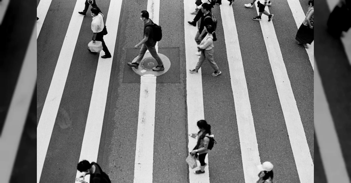 Pedone con smartphone in mano attraversa sulle strisce, illustrazione del nuovo Codice della Strada con multa da 75 euro.