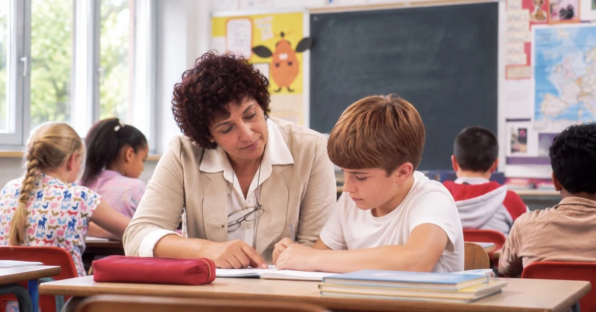 Insegnante seduta accanto a un alunno in un'aula scolastica luminosa